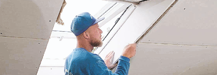 Ein Handwerker verkleidet die Seiten eines Dachfensters mit Gipskarton.